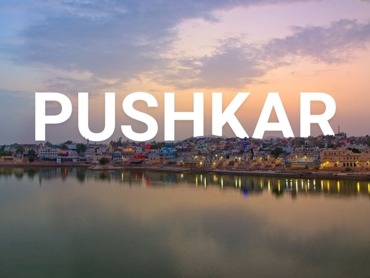 Crowd of pilgrims, camels, and stalls at Pushkar Fair amid desert landscape under clear blue sky